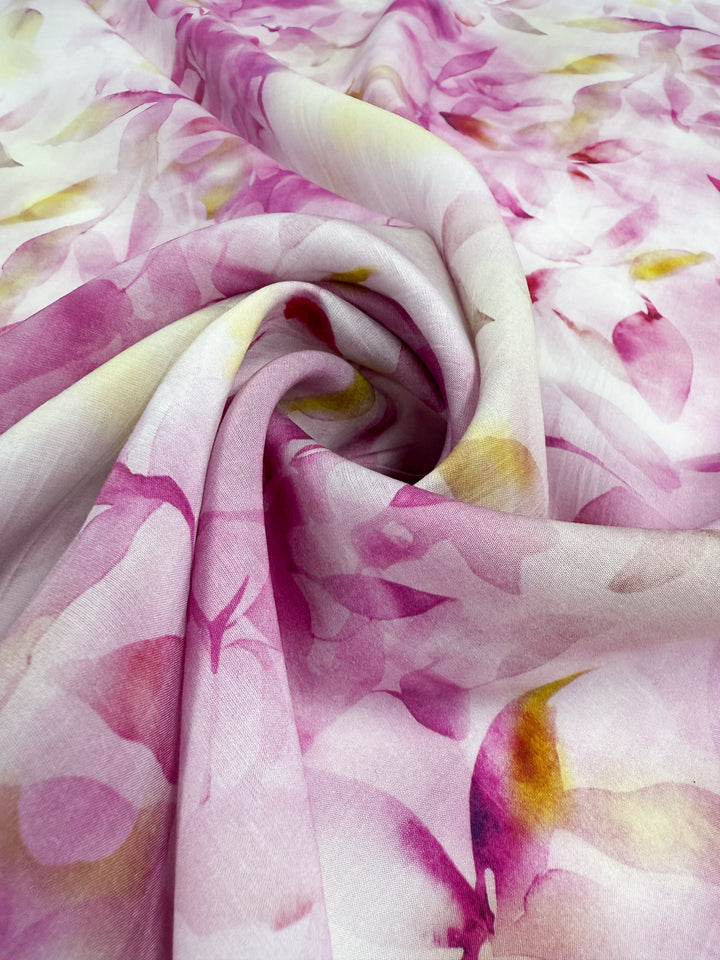 Designer Cotton - Bloom Drift by Super Cheap Fabrics features soft, lightweight cotton (145cm wide) with a swirl pattern and watercolor floral prints in pink, purple, and yellow, draping smoothly with gentle folds.