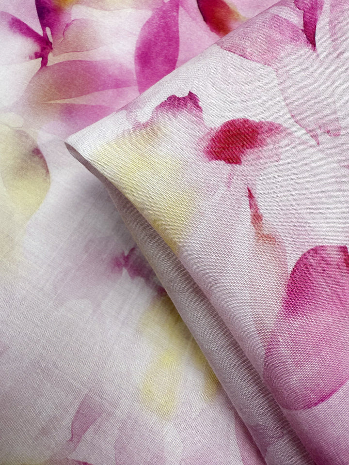 Close-up of Designer Cotton - Bloom Drift by Super Cheap Fabrics, 145cm wide. This luxury lightweight cotton fabric in light pink features a watercolor floral pattern in pink, purple, and yellow on both sides.