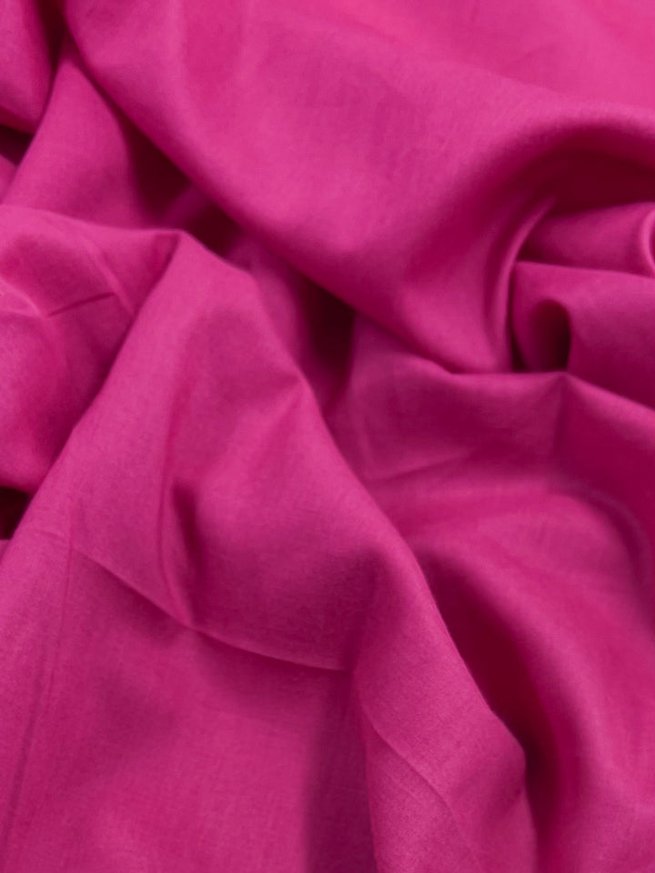 A close-up showcases the textured elegance of Super Cheap Fabrics' Cotton Voile in Fuchsia, 145cm wide, featuring soft folds and wrinkles that enhance its vibrant color and delicate smoothness.