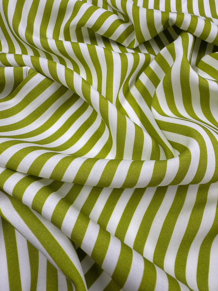 A close-up of Super Cheap Fabrics' Printed Rayon - Lime Pop Stripe (140cm), featuring green and white diagonal stripes with wavy folds that create an optical illusion on this lightweight fabric.