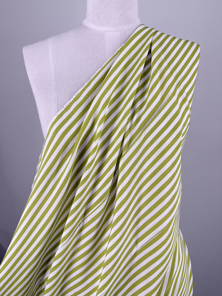 A mannequin wears Super Cheap Fabrics' Printed Rayon - Lime Pop Stripe (140cm), featuring green and white diagonal stripes, draped over one shoulder against a plain light background.