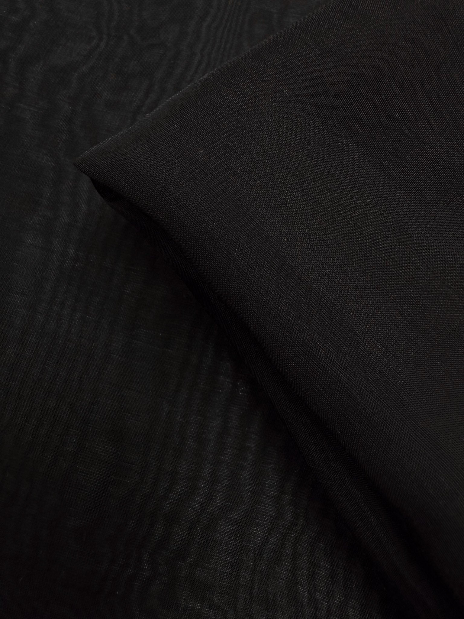 A close-up of Super Cheap Fabrics' Designer Voile - Black - 150cm displays its smooth, lightweight texture and subtle folds, with one section neatly folded over another.