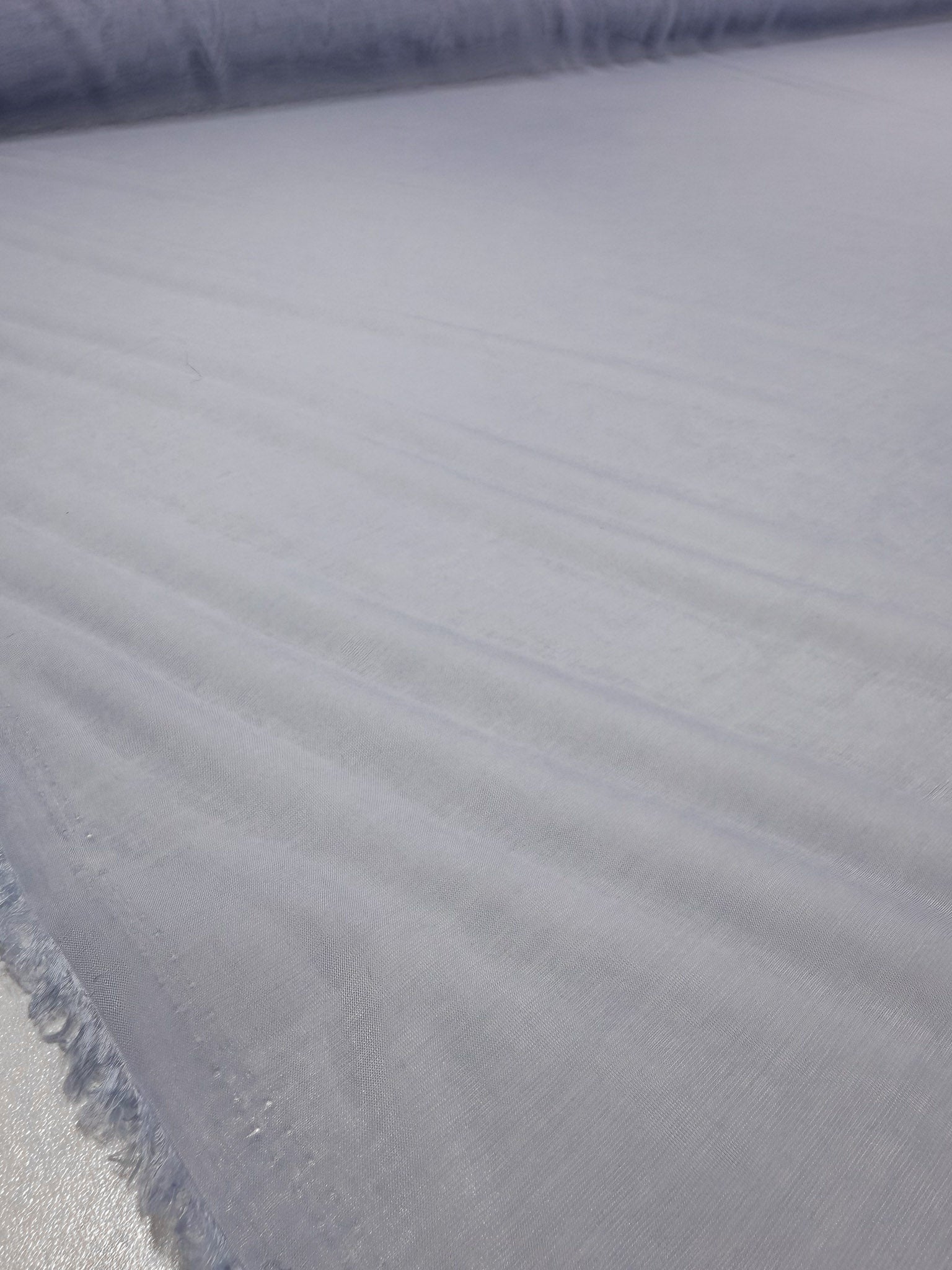 A close-up of Super Cheap Fabrics' Designer Voile - Skywriting - 150cm shows its smooth, light purple lightweight fabric with soft folds and frayed edges along the left side.