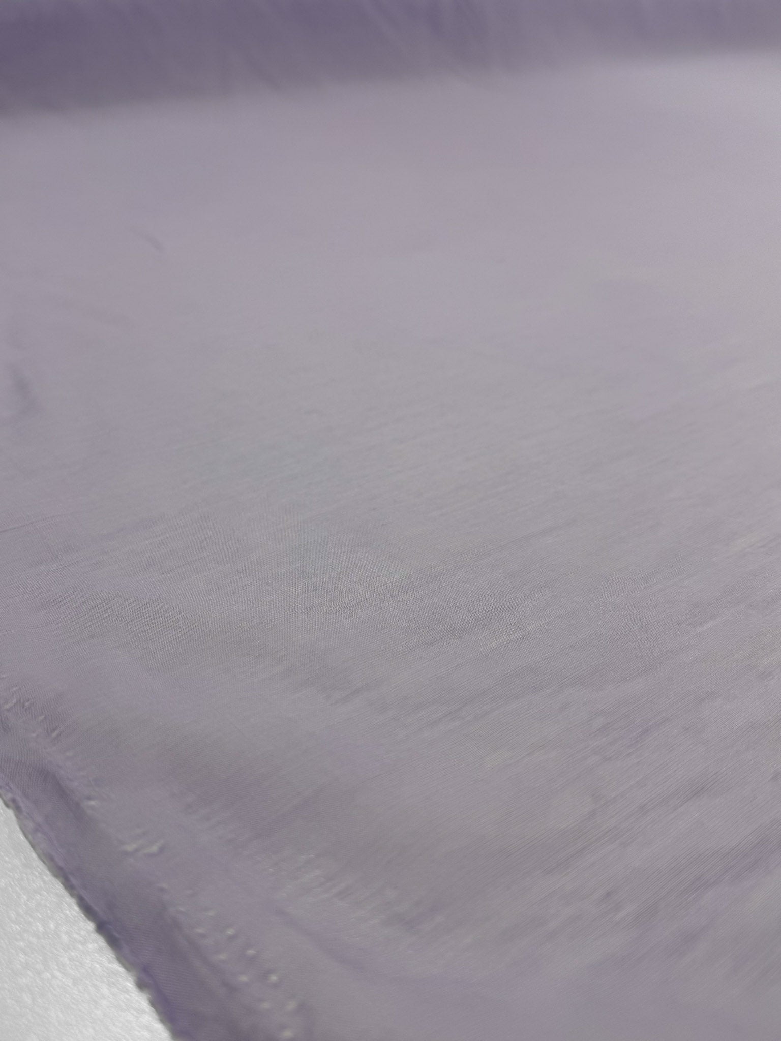 A close-up of Designer Voile - Pastel Lilac - 150cm by Super Cheap Fabrics shows its lightweight cotton texture and subtle folds, emphasizing the fabric's delicate look.
