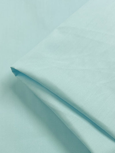 A neatly folded piece of "Cooling Spray" light blue poplin (148cm) from Super Cheap Fabrics rests on a matching background, ideal for crafting charming childrenswear.