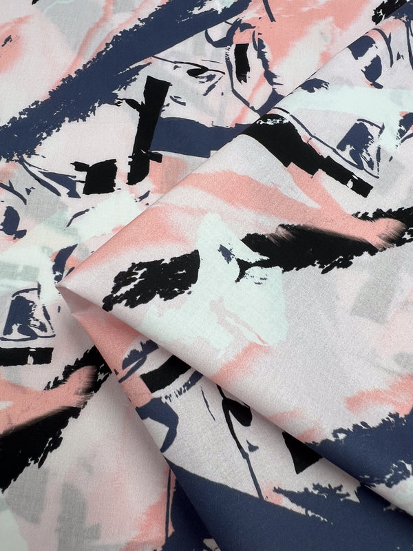 The Super Cheap Fabrics' "Printed Cotton - Peaches & Cream - 150cm" features an abstract pattern of black, white, and pink brushstrokes on a lightweight cotton fabric for a modern artistic design.