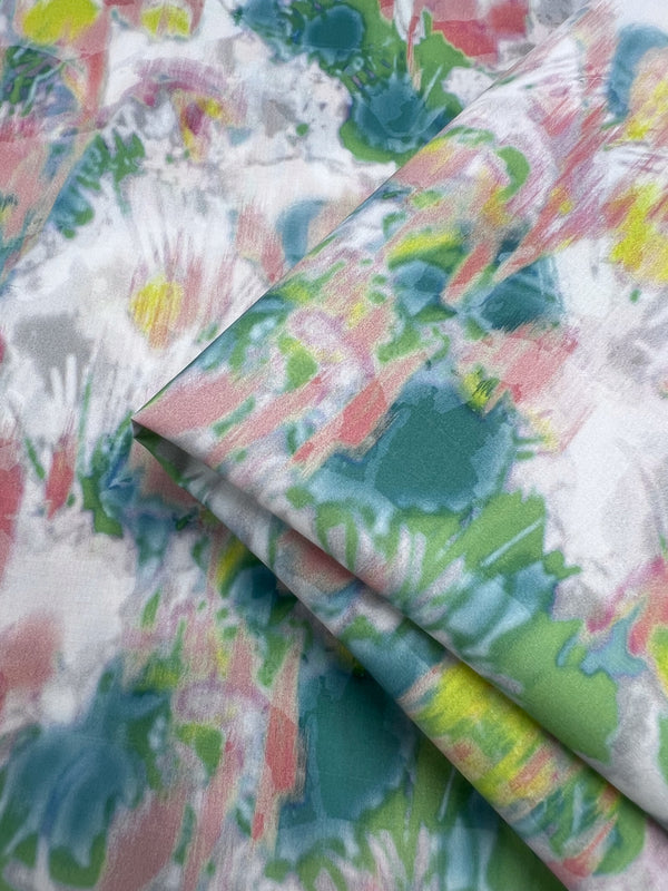 Close-up of the Super Cheap Fabrics' Printed Cotton - Terrain - 150cm displaying a vibrant abstract pattern with splashes of teal, pink, yellow, and white. The lightweight cotton's natural fibers create a colorful, dynamic appearance with a soft and delicate feel.