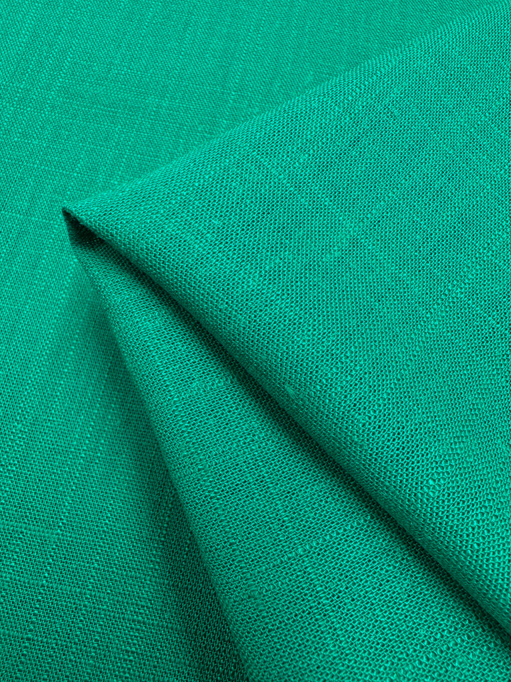 A close-up of folded Super Cheap Fabrics' Linen Blend - Sea Green - 135cm with a slightly textured weave. The fabric's vibrant color and pattern are accentuated by the fold, highlighting its smooth yet slightly coarse surface—perfect for table linens.