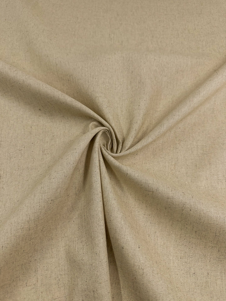 Close-up of a piece of Super Cheap Fabrics' Linen Blend - Short Bread - 135cm with a plain weave, gathered in the middle into a small spiral. The fabric appears smooth and slightly textured, with natural-looking speckles. The spiral creates gentle folds and shadows, adding dimension to the image.