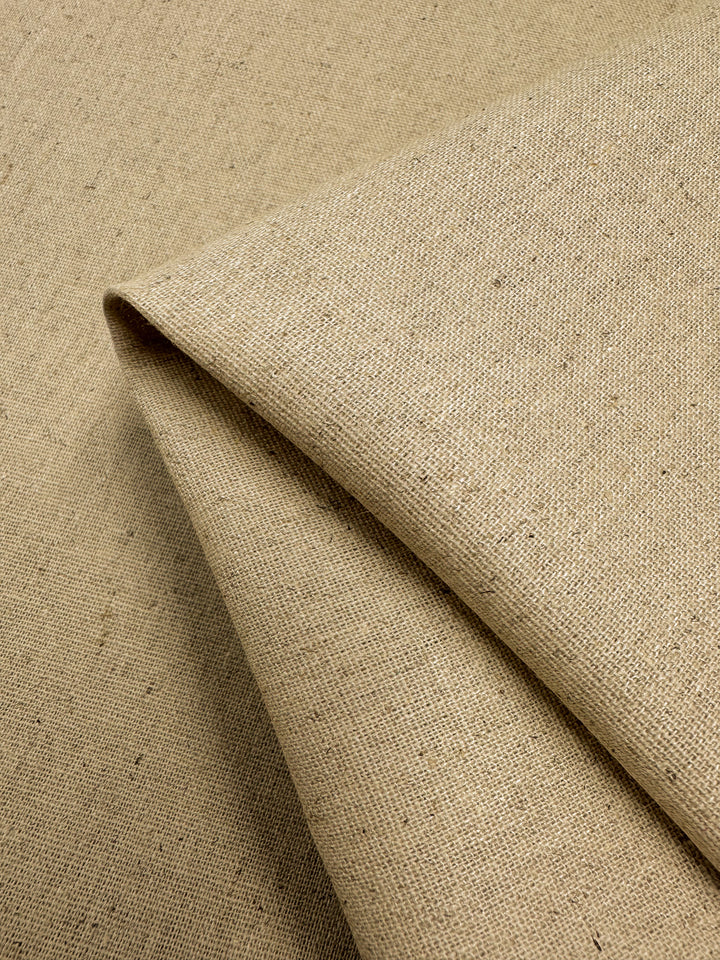 A close-up of Super Cheap Fabrics' Linen Blend - Short Bread - 135cm. The fabric is slightly folded, showing its coarse texture and natural weave with minor imperfections, giving it a rustic appearance reminiscent of lightweight linen table linens.