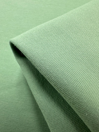 Close-up of Super Cheap Fabrics' Cotton Lycra - Spruce Stone - 170cm, folded to highlight its soft, finely woven texture. The stretchy fabric's smooth look and gentle shadows emphasize its flexibility, perfect for bodycon dresses.