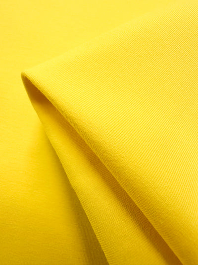 Close-up of Super Cheap Fabrics' Cotton Lycra in Vibrant Yellow, 170cm. Its smooth, soft texture is highlighted by the fabric's neat folds and uniform surface.