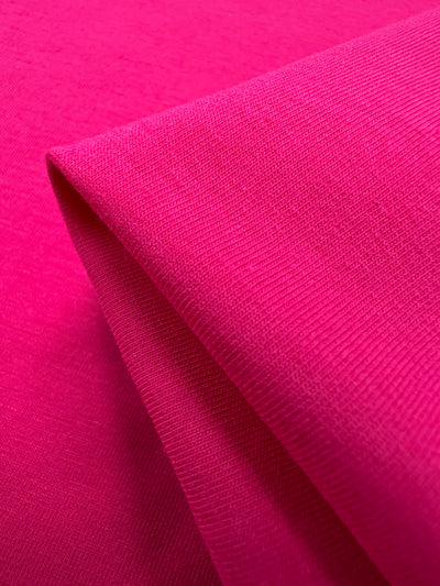 Close-up of the vibrant Super Cheap Fabrics' Cotton Lycra in Fandango Pink, 160cm wide, highlighting its textured surface and neatly folded edge with an interplay of light and shadow—ideal for crafting stylish bodycon dresses.