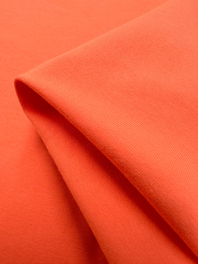 Close-up of a folded piece of Super Cheap Fabrics' Cotton Lycra in Fusion Coral, 170cm wide, highlighting its smooth texture and draping quality.