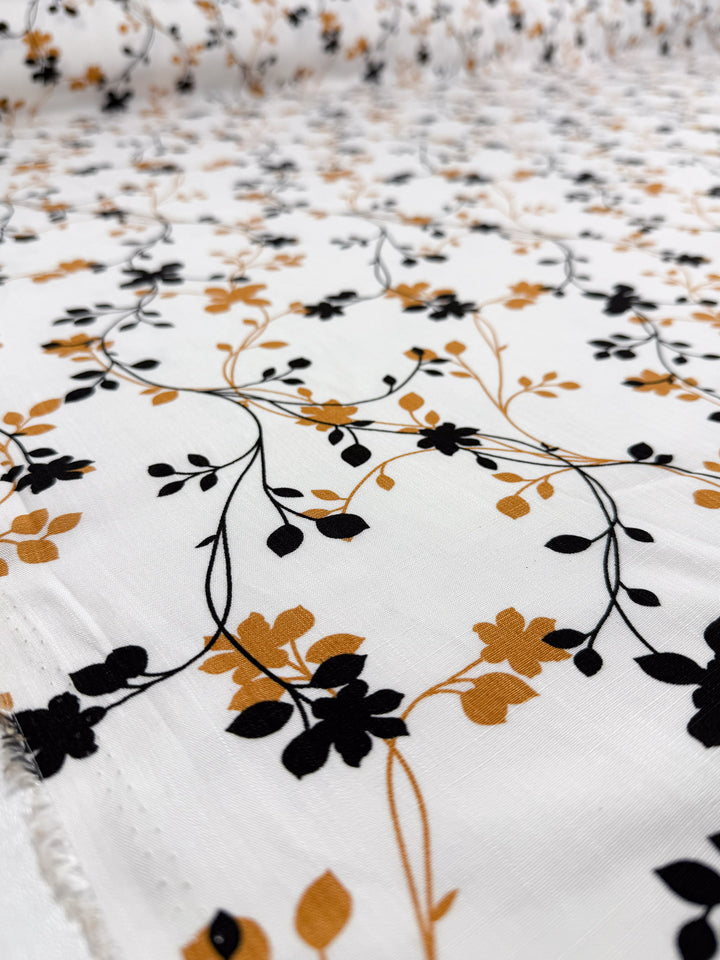 The Bamboo Rayon - Vine Whisper by Super Cheap Fabrics features a lightweight 150cm fabric with black and mustard-yellow floral vine patterns, including delicate flowers and leaves across the surface.