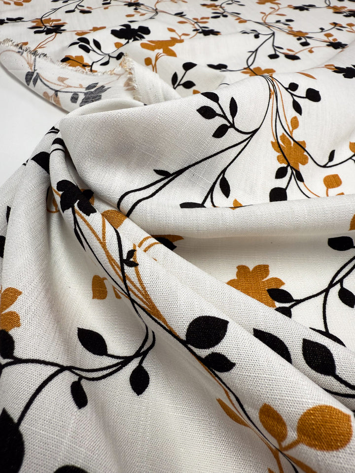 Super Cheap Fabrics’ Bamboo Rayon - Vine Whisper (150cm) features a black and mustard yellow floral and leaf print on soft white fabric. Lightweight, loosely draped, and ideal for beginner-friendly sewing projects.