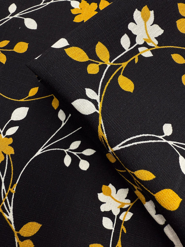 Super Cheap Fabrics’ Bamboo Rayon - Golden Vine (150cm) features a black base with white and yellow flowers, winding stems, and leaves. This lightweight fabric’s floral design is perfect for beginner-friendly sewing projects.