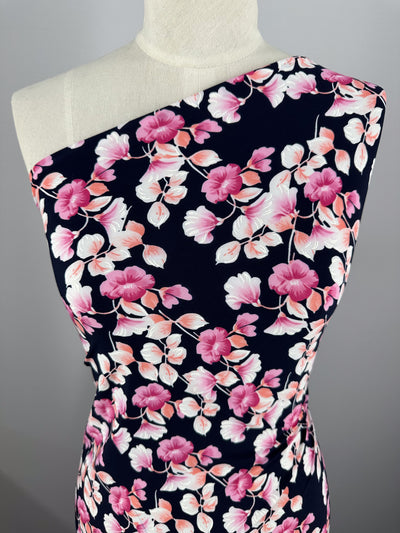 A dress form showcases a sleeveless dress made from medium-weight Textured Lycra - Puff by Super Cheap Fabrics, featuring a dark blue background with pink and white floral patterns. The dress has an asymmetrical neckline for added flair.