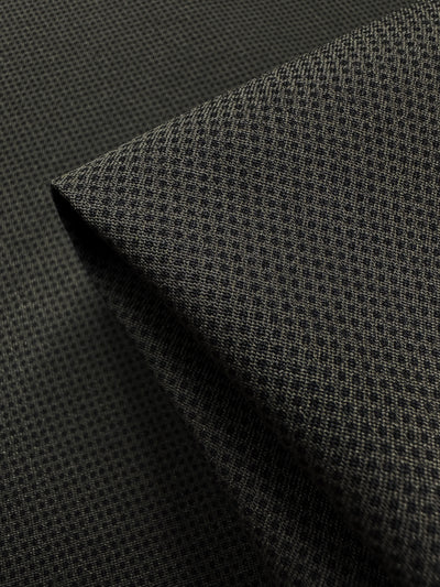 A close-up of Super Cheap Fabrics' Printed Bengaline - Pin Dot Khaki showcases a dark green, medium-weight fabric with small square patterns. Its soft texture and nuanced design highlight the woven detail in an elegant, neatly folded 150cm piece.