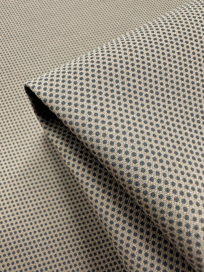 Close-up of Super Cheap Fabrics' Printed Bengaline - Pin Dot Sand (150cm) fabric, a medium-weight stretch material with small black dots on beige. It's folded into a triangular crease, enhancing texture and depth.