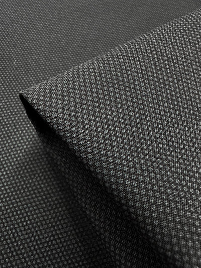 A close-up of folded Printed Bengaline - Pin Dot Black fabric by Super Cheap Fabrics, ideal for skirts and dresses. The medium-weight texture appears soft, revealing the detailed weave design. Width: 150cm.