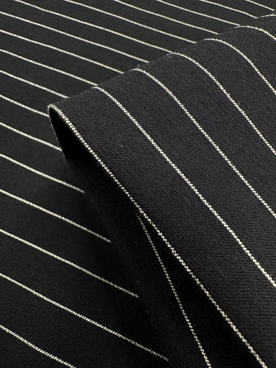 Close-up of the Super Cheap Fabrics' Printed Bengaline in Ivory Pin Stripe, 145cm. The black stretch fabric features finely spaced white stripes, ideal for skirts, dresses, pants, shorts, or jackets with its smooth and medium-weight texture.