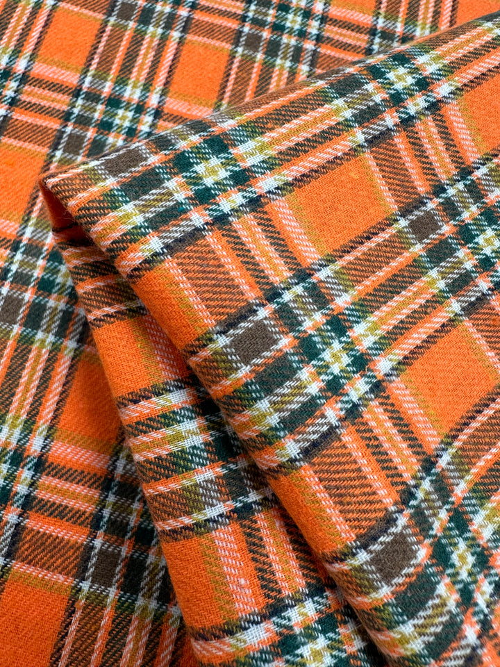 Close-up of Super Cheap Fabrics’ versatile "Suiting - Orange Glen Check - 147cm," showcasing a vibrant plaid pattern with intersecting orange, green, white, and brown stripes that create a checkerboard design. The lightweight fabric has a warm and cozy appearance.