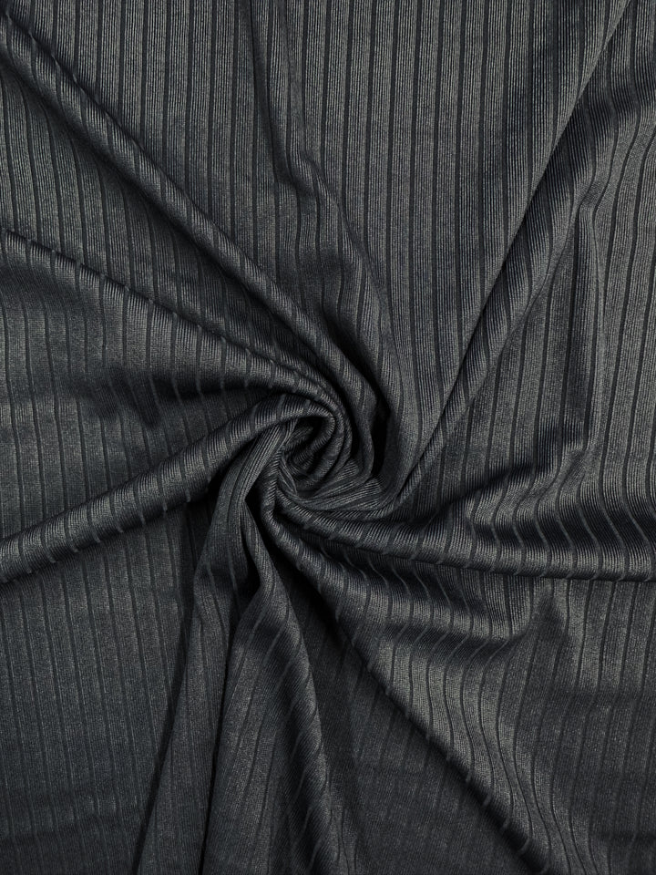 A close-up of Super Cheap Fabrics' "Rib Knit - Total Eclipse - 168cm" shows a dark gray, medium weight fabric with a swirling pattern. Its soft texture features tightly spaced vertical ridges for added depth.