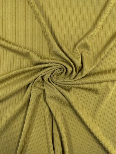 The Rib Knit - Avocado Oil by Super Cheap Fabrics features a close-up of its olive-green ribbed fabric, artistically twisted into a central spiral. This medium-weight knit shows parallel lines, offering a dynamic look with stretchy comfort. Width: 173cm.