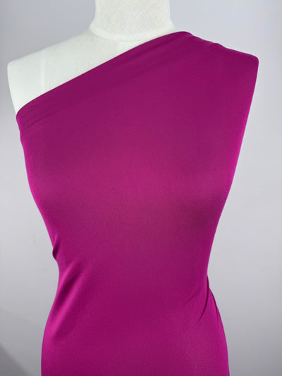 A mannequin displays an elegant one-shoulder dress made from Super Cheap Fabrics' Cotton Lycra in Festival Fuschia. The smooth, form-fitting design exudes sophistication against a neutral gray background.