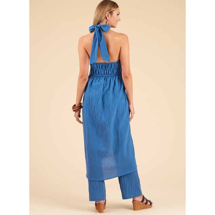 A woman is seen from behind wearing a sleeveless outfit made from the New Look 6736 pattern for misses' tops and trousers by Super Cheap Fabrics. The blue design features a halter neck tie, complementing her long, loose hair. She completes the look with wedge sandals and bracelets against a simplistic beige background.