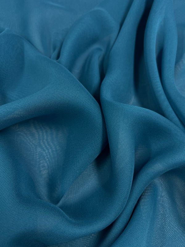 A close-up image of the crinkled, sheer Silk Georgette - Celestial from Super Cheap Fabrics. The material appears lightweight and soft, with delicate folds creating shadows and varying shades of blue throughout. The texture seems smooth and slightly translucent, perfect as a lightweight spring-summer fabric.