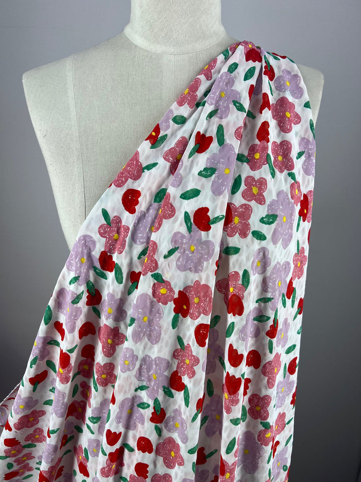 A mannequin displays the elegant Daise fabric by Super Cheap Fabrics, featuring vibrant salt shrunk prints on a white backdrop adorned with colorful pink, red, and purple flowers and green leaves.