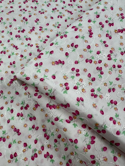 The "Embroidered Printed Cotton - Posy" by Super Cheap Fabrics features a white lightweight fabric adorned with a floral pattern of small pink flowers, green leaves, and yellow accents. Made from natural cotton fibers, this 112cm wide fabric is slightly folded to reveal a subtle textured design with delicate embroidery details.