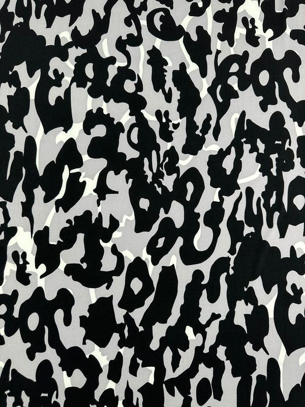 The Printed Lycra - Camo - 150cm fabric from Super Cheap Fabrics features a black, white, and grey abstract camouflage pattern. This medium-weight Polyester/Spandex fabric is adorned with irregular, organic shapes that scatter across its surface, creating a highly contrasting and fragmented appearance. The design's random and chaotic arrangement evokes a sense of dynamic movement.