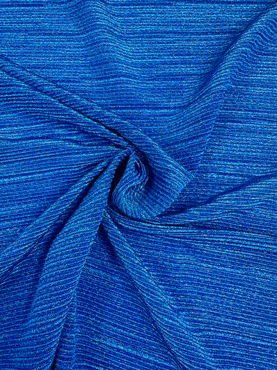 A close-up of the "Metallic Knit - Cobalt - 150cm" from Super Cheap Fabrics reveals a stunning cobalt knit fabric with fine, horizontal lines in varying shades of blue. The medium to heavy weight fabric is artfully draped in a swirl pattern at the center, creating a textured and dynamic appearance. The overall texture appears soft and slightly shimmery.