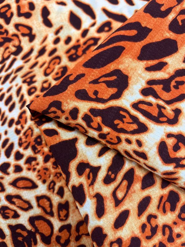 Close-up of the Deluxe Print - Jungle Tides - 155cm polyester fabric by Super Cheap Fabrics, showcasing a vibrant orange and black leopard print pattern that resembles genuine leopard fur. Multiple layers of this versatile fabric are displayed, emphasizing its smooth texture and striking contrast of colors.