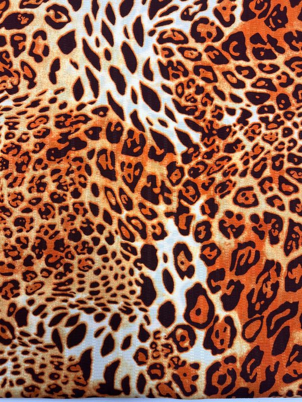 A close-up image of the Deluxe Print - Jungle Tides - 155cm fabric by Super Cheap Fabrics. This polyester fabric boasts a captivating leopard print pattern with diverse shades of orange, black, and white, artfully replicating the natural spots of a leopard's fur. Its bold and versatile appearance makes it ideal for designer fabrics.