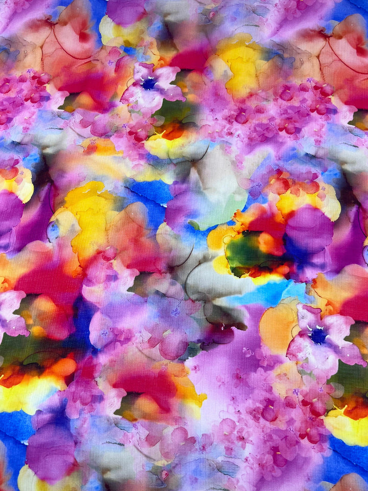 The Designer Cotton - Wonder - 150cm by Super Cheap Fabrics showcases a vibrant abstract watercolor design. It features a blend of bright colors like pink, purple, yellow, blue, and orange with organic shapes and smooth transitions for a floral pattern reminiscent of high-end textile art.