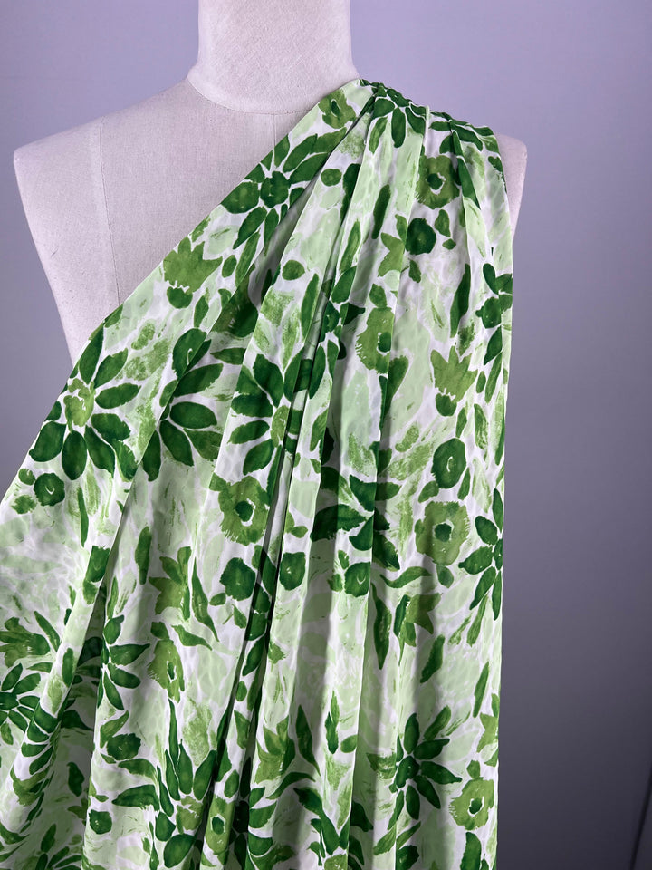 A mannequin showcases the vibrant green and white floral pattern of the Edelweiss fabric (155cm) by Super Cheap Fabrics, enhanced by Salt Shrunk Prints with leaves and flowers for a lively look.