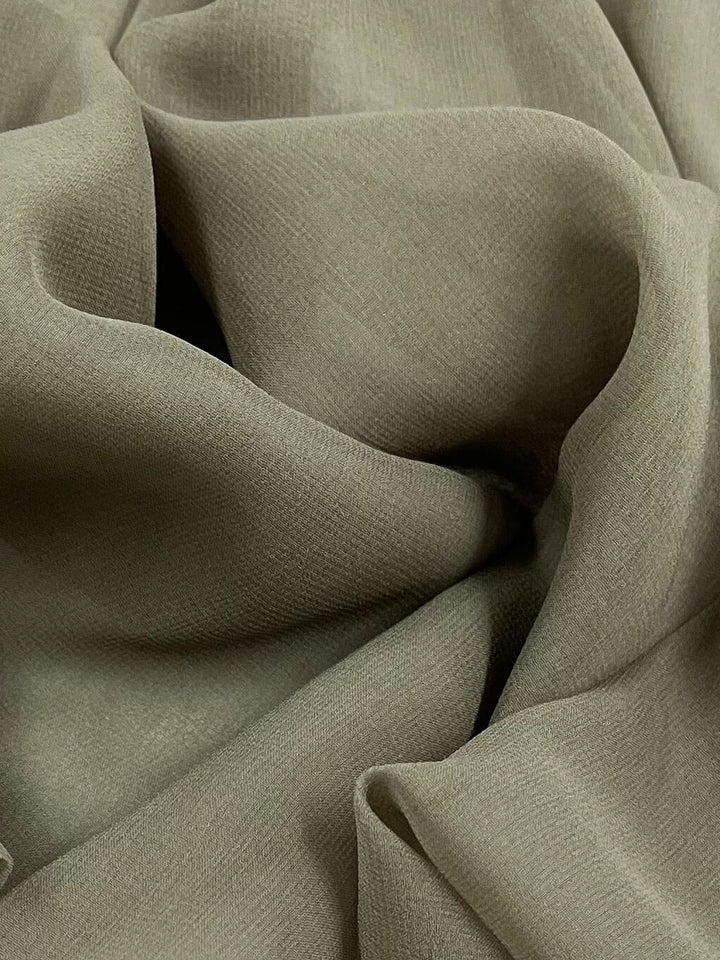 A close-up of Super Cheap Fabrics' Pure Silk Georgette - Dune (135cm) in olive green, showcasing its soft, textured appearance and gentle folds that form a flowing, wave-like pattern. Perfect for lightweight spring and summer outfits.