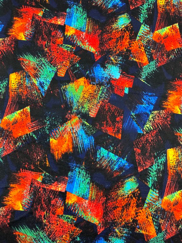 The Textured Knit - Art Attack - 155cm fabric by Super Cheap Fabrics showcases a vibrant abstract pattern with bold brush strokes in shades of red, orange, blue, green, and yellow. The colors blend and overlap on a dark background, creating a chaotic yet visually engaging and dynamic effect that mimics the look of textured knit fabrics.