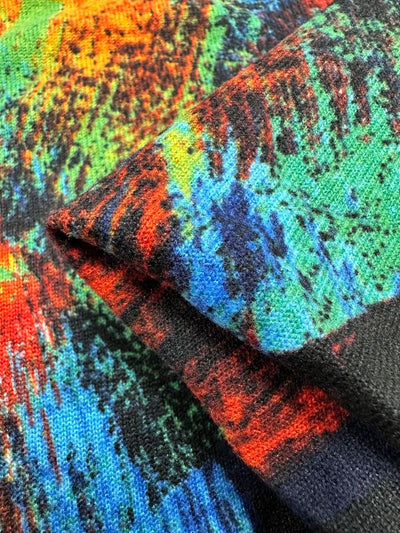 Close-up of the Textured Knit - Art Attack - 155cm by Super Cheap Fabrics, featuring vibrant patterns in red, blue, green, and orange hues. The detailed design of the generously stretchy fabric is visible, with part of it folded over to reveal its rich colors and intricate texture.