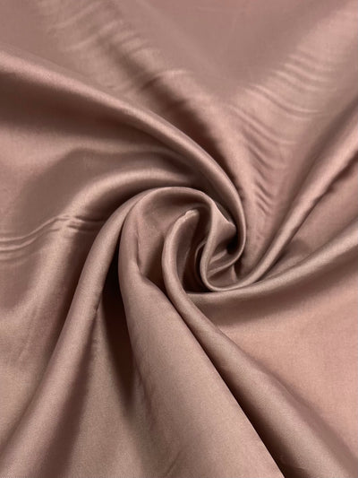 A close-up view of a smooth, silky fabric in a soft dusty rose color. The vibrant fabric has gentle folds and a slight sheen, creating a luxurious and elegant appearance. This is the Lining - Aragon - 120cm by Super Cheap Fabrics.