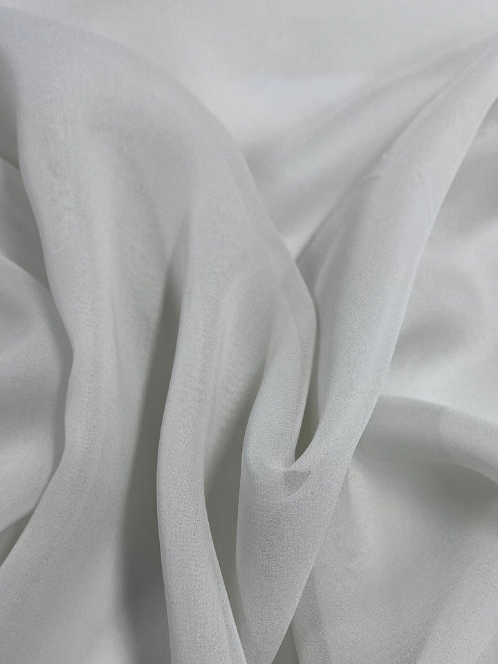 A close-up of Super Cheap Fabrics' Pure Silk Georgette in Silver Blue, 135cm wide, draped in folds, highlights its smooth texture and light, translucent quality. This lightweight fabric is perfect for elegant spring and summer outfits.