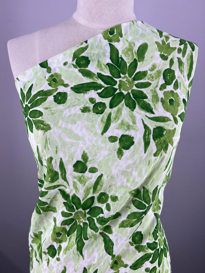 A mannequin draped in Salt Shrunk Print - Edelweiss by Super Cheap Fabrics, featuring a vibrant green floral pattern on a white background. The design showcases lush green shades, enhancing the vibrant tones.