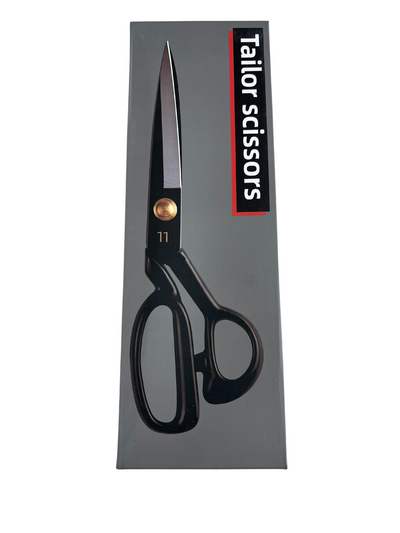A box of Super Cheap Fabrics Tailor Scissors - Dressmaking Shears featuring a picture of the scissors on the front. The scissors, crafted from durable manganese steel, have a sleek black handle and metal blades. The text "Tailor Scissors - Dressmaking Shears" in white and red is displayed vertically on the right side of the box.