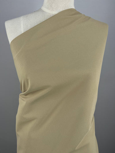 A mannequin dressed in a single-shoulder, draped Delustered Satin - Pale Khaki - 150cm against a plain gray background. The Super Cheap Fabrics polyester material smoothly covers the front of the mannequin, highlighting the texture and elegant drape of the fabric.