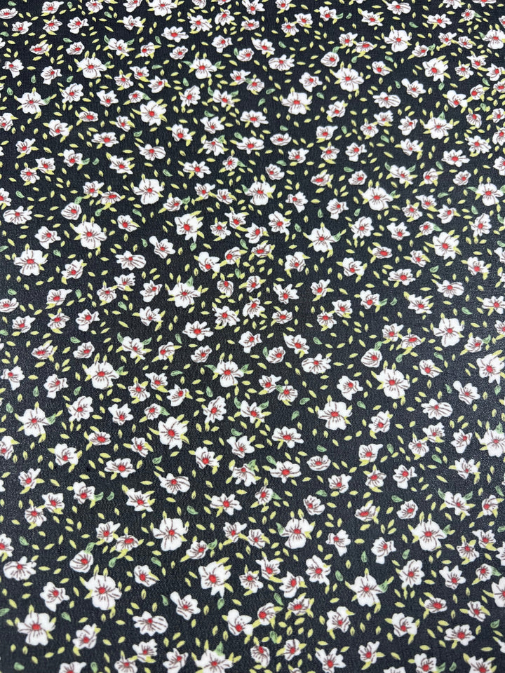 A close-up of the Printed Georgette - Dark Blooming Seeds from Super Cheap Fabrics, showcasing its delicate floral pattern with small white flowers featuring red centers and green leaves set against a black background.