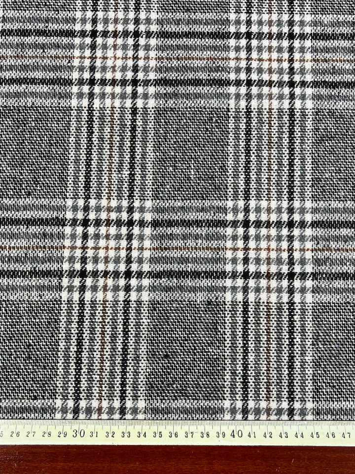 Close-up of the Super Cheap Fabrics Wool Flannel - Nuthatch Plaid. The black, white, and gray plaid fabric is shown with a ruler measuring in both centimeters and inches along the bottom edge. This high-quality 150 cm wool-blend features intersecting lines forming squares while the ruler provides a scale reference for the fabric's design, perfect for winter pants.